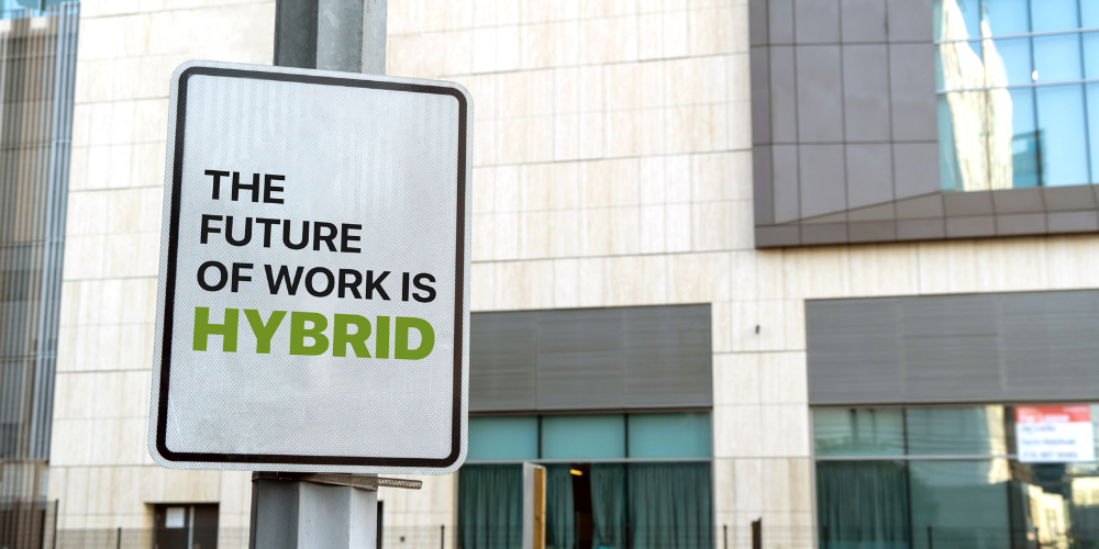 Street sign against an urban building backdrop with the message 'THE FUTURE OF WORK IS HYBRID', emphasizing the evolving nature of modern workplaces.