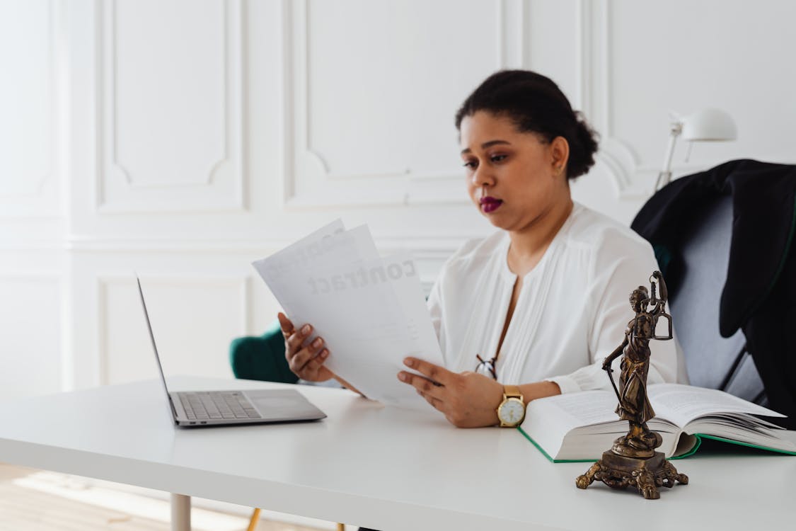 A focused HR professional reviewing documents with a laptop and a justice scale statue on the desk, symbolizing the balance in staaffing costs.
