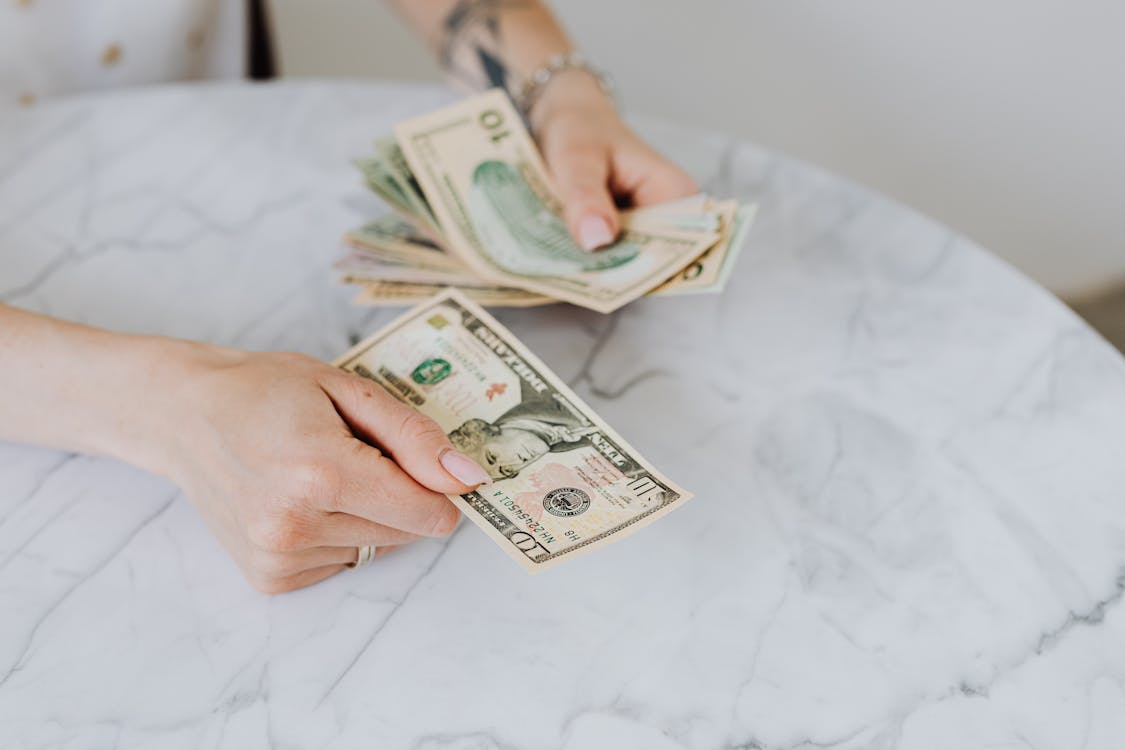 Hands of a person counting a stack of US dollar bills on a marble surface, signifying the financial aspects of staffing.
