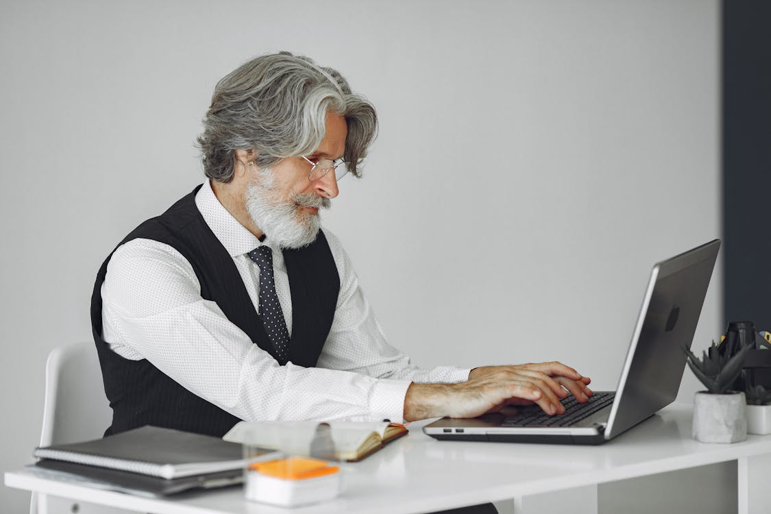 A focused senior businessman analyzing data on a laptop in an office setting, relevant to cost analysis and hiring strategies.