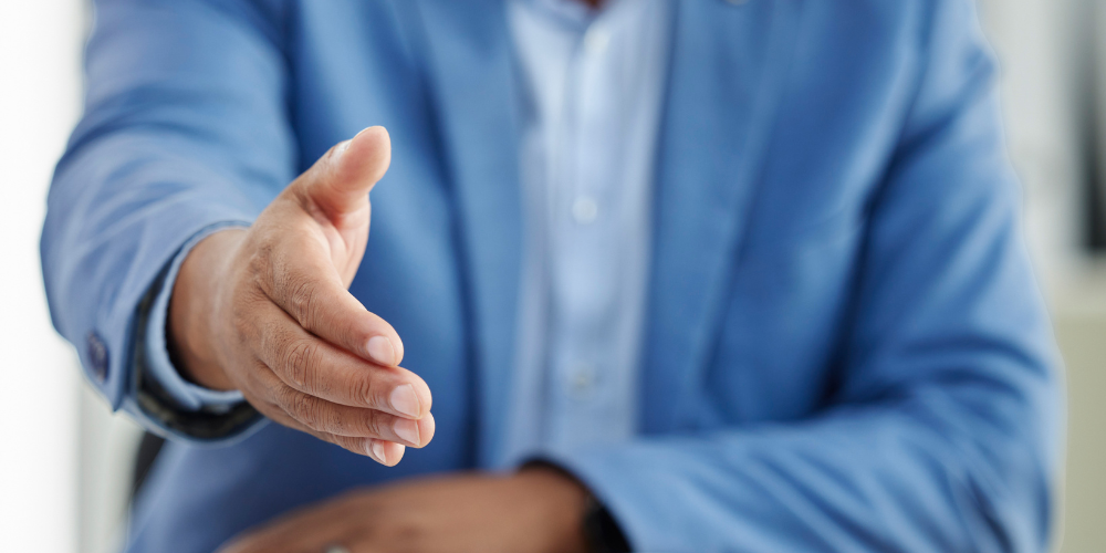 A person in a blue blazer extending a welcoming handshake, symbolizing an inviting and professional onboarding process.