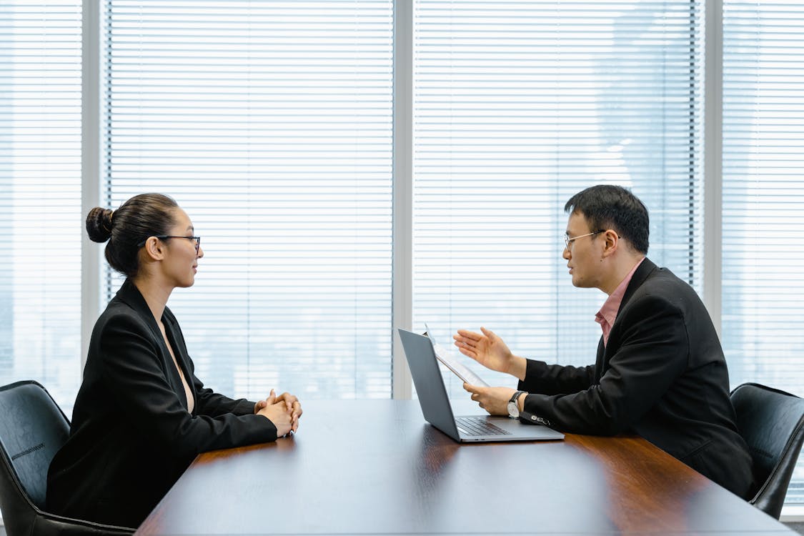 Two Professionals in a Business Meeting with Laptop in a Modern Office with Blinds.