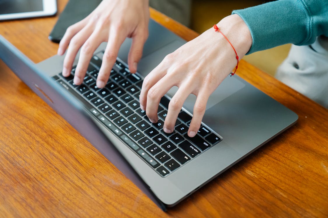 Hands Typing on the Keyboard of a Laptop on a Wooden Desk.