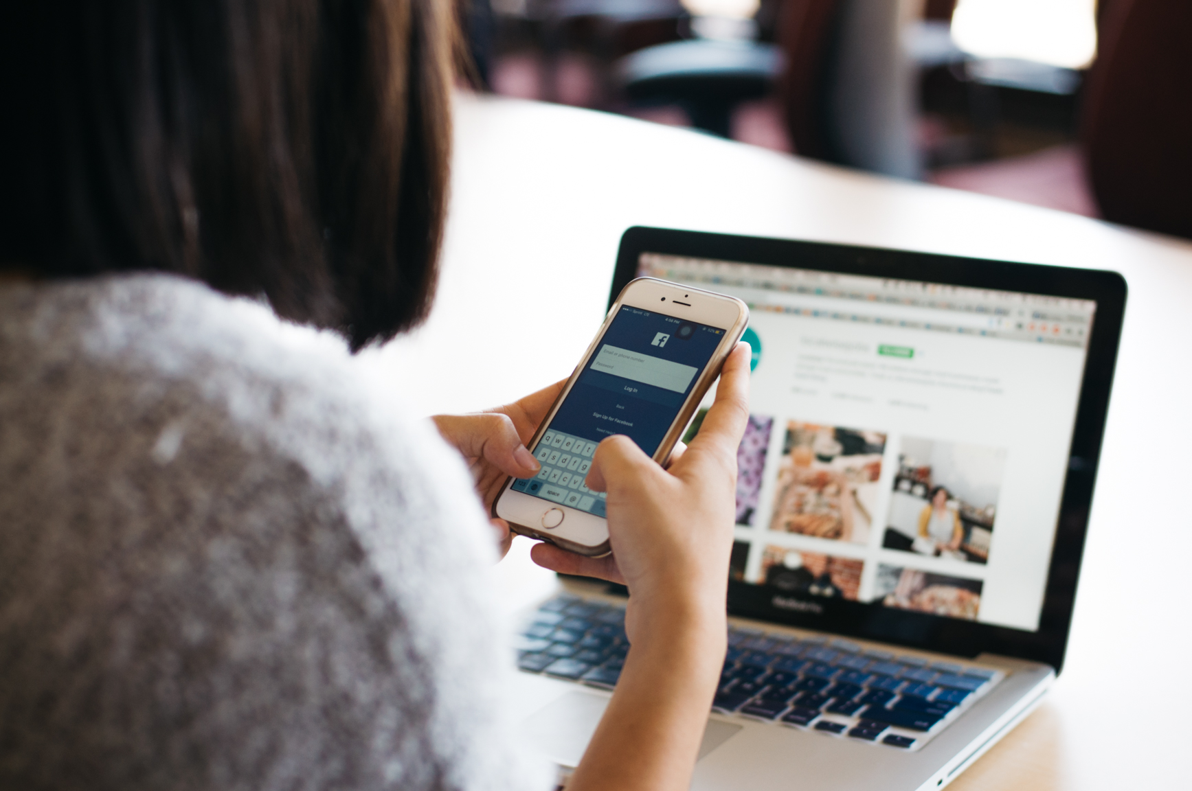 Person Using Smartphone with Laptop Open in the Background.