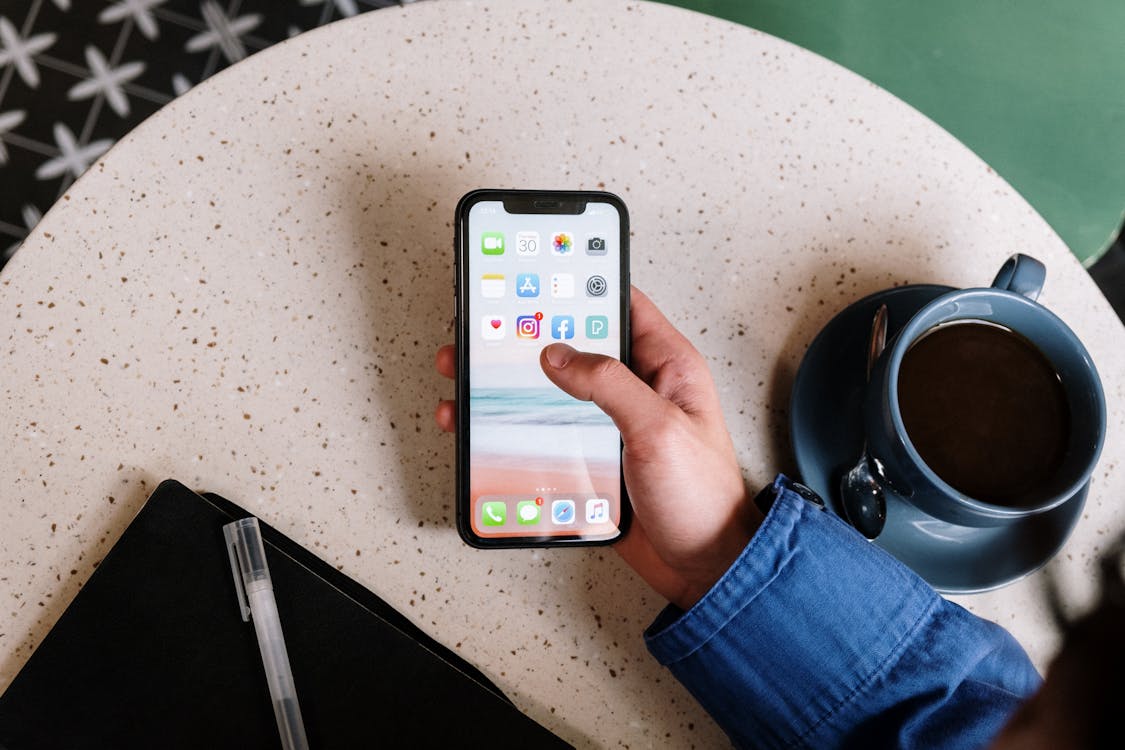 Person Holding a Smartphone Above a Table with a Cup of Coffee.