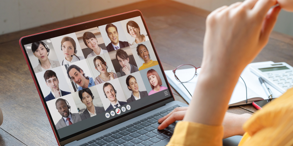 Over-the-shoulder view of a person participating in a virtual meeting with diverse colleagues displayed on a laptop screen.