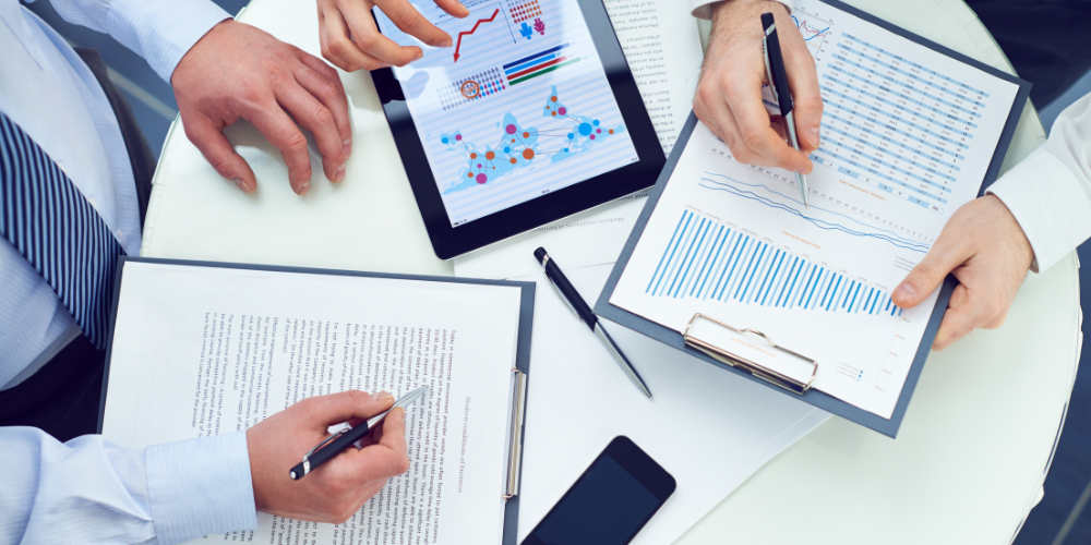 Business professionals analyzing financial documents, charts, and data on digital tablets and paper, collaborating over a table.