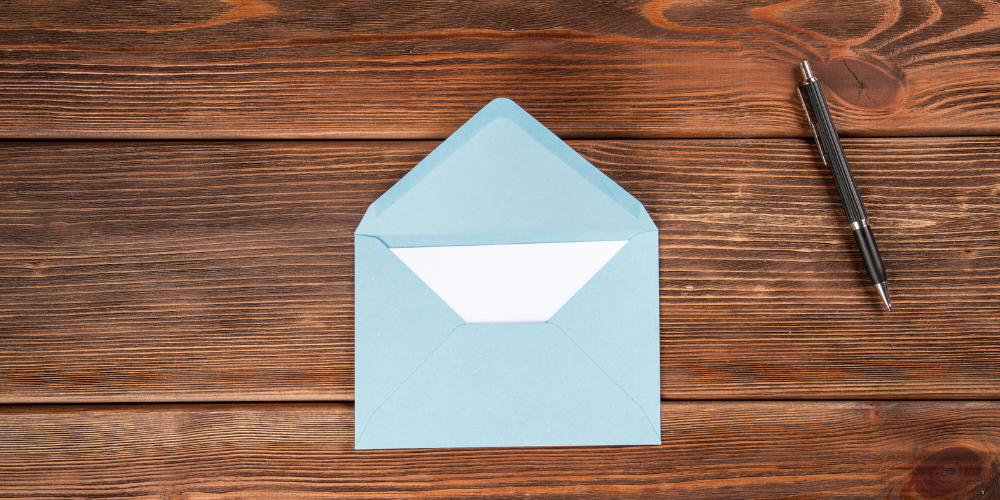 A light blue open envelope on a dark wood surface with a white piece of paper peeking out, next to a black pen on the right side.