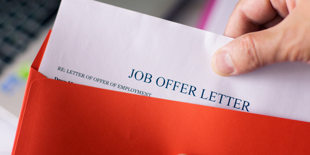 A hand opening a red envelope with a job offer letter inside