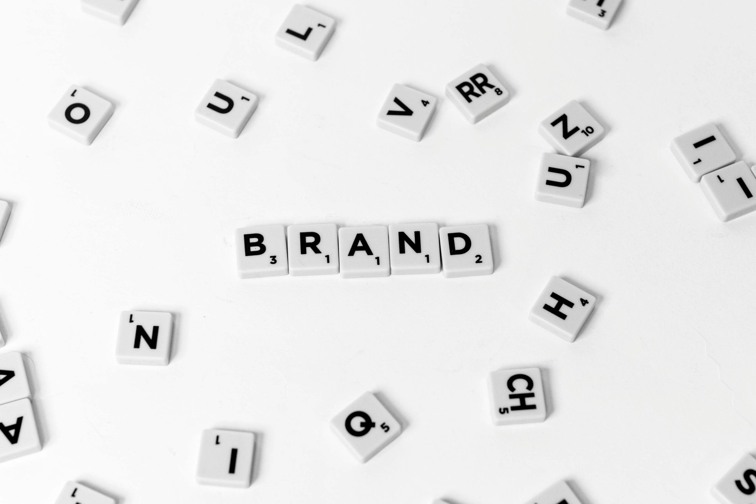 Scrabble tiles spelling out 'BRAND' amidst scattered letters on a white background.
