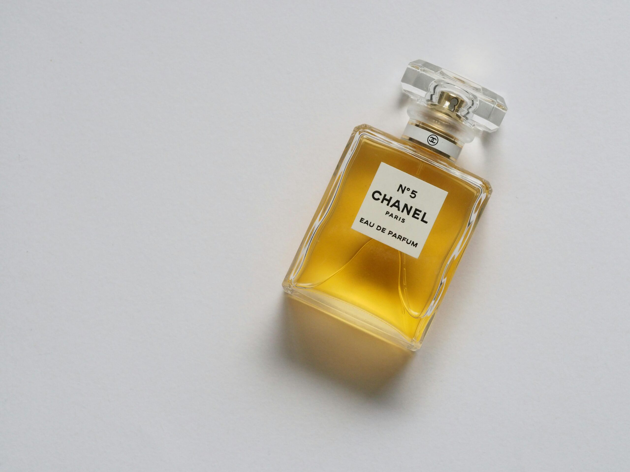 A clear glass bottle of Chanel No. 5 perfume with a square base and a faceted cap, filled with yellow perfume liquid, set against a plain white background.