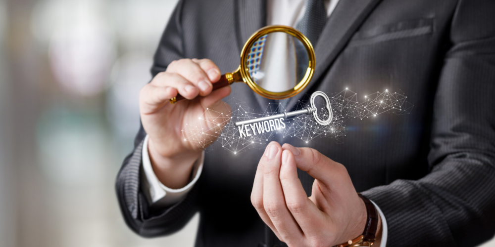 The image shows a person in a business suit holding a magnifying glass close to a set of digital keywords that are highlighted and connected by network-like lines, suggesting a concept of searching or focusing on keywords, likely in the context of digital marketing or search engine optimization.