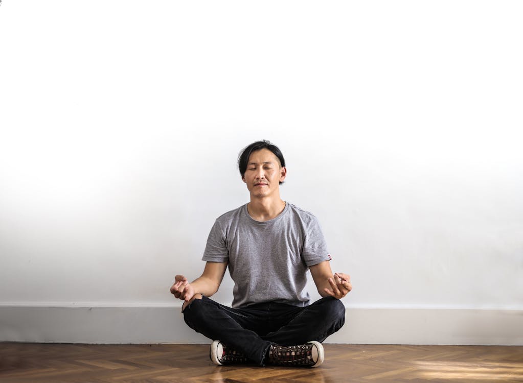 Gratis Foto De Hombre En cam-velascoiseta Gris Y Jeans Negros Sentado En Un Piso De Madera Meditando Foto de stock