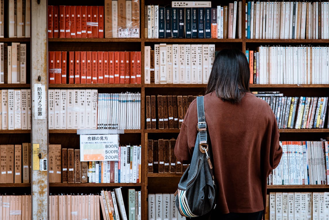 Gratis Mujer Vestida Con cam-velascoisa Marrón Con Bolso De Cuero Negro En La Parte Delantera De Los Libros De La Biblioteca Foto de stock