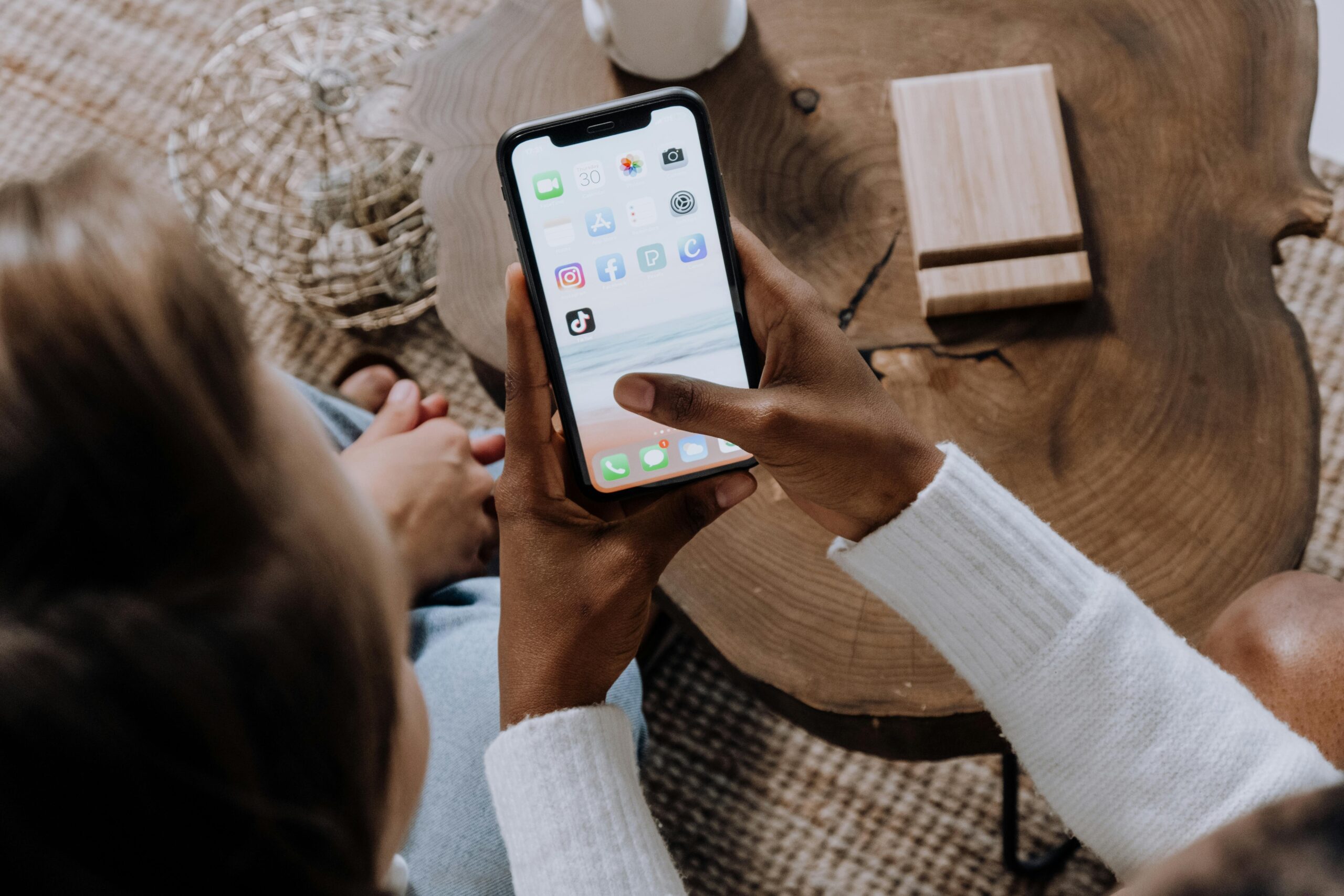 Close-up of a person holding a smartphone with various app icons on the screen, over a wooden table.