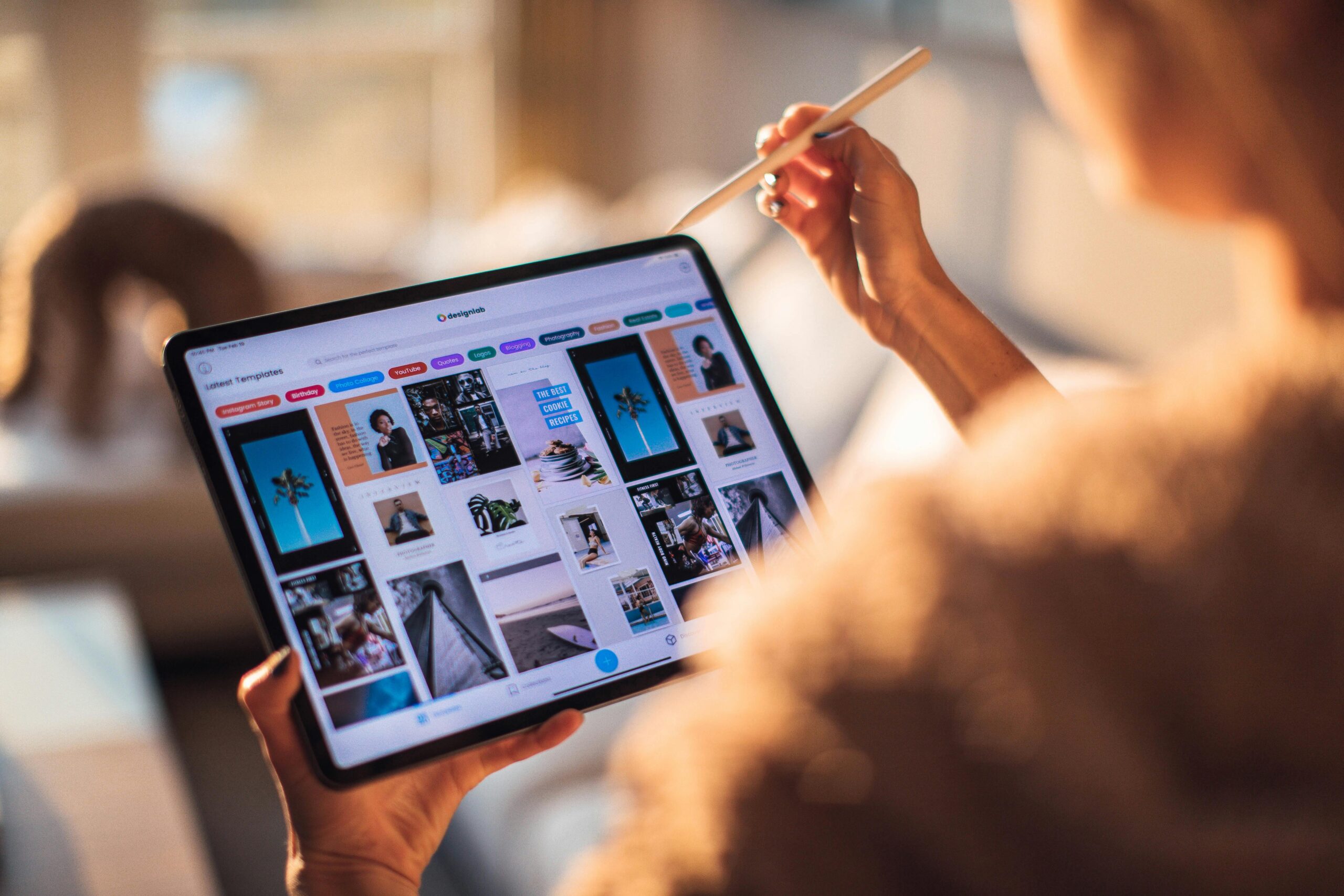 A person holding a digital tablet with a stylus, browsing through a gallery of design templates.