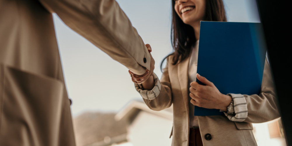 A handshake between two professionals in an office setting, one of them holding a folder, possibly after a successful job interview or meeting.