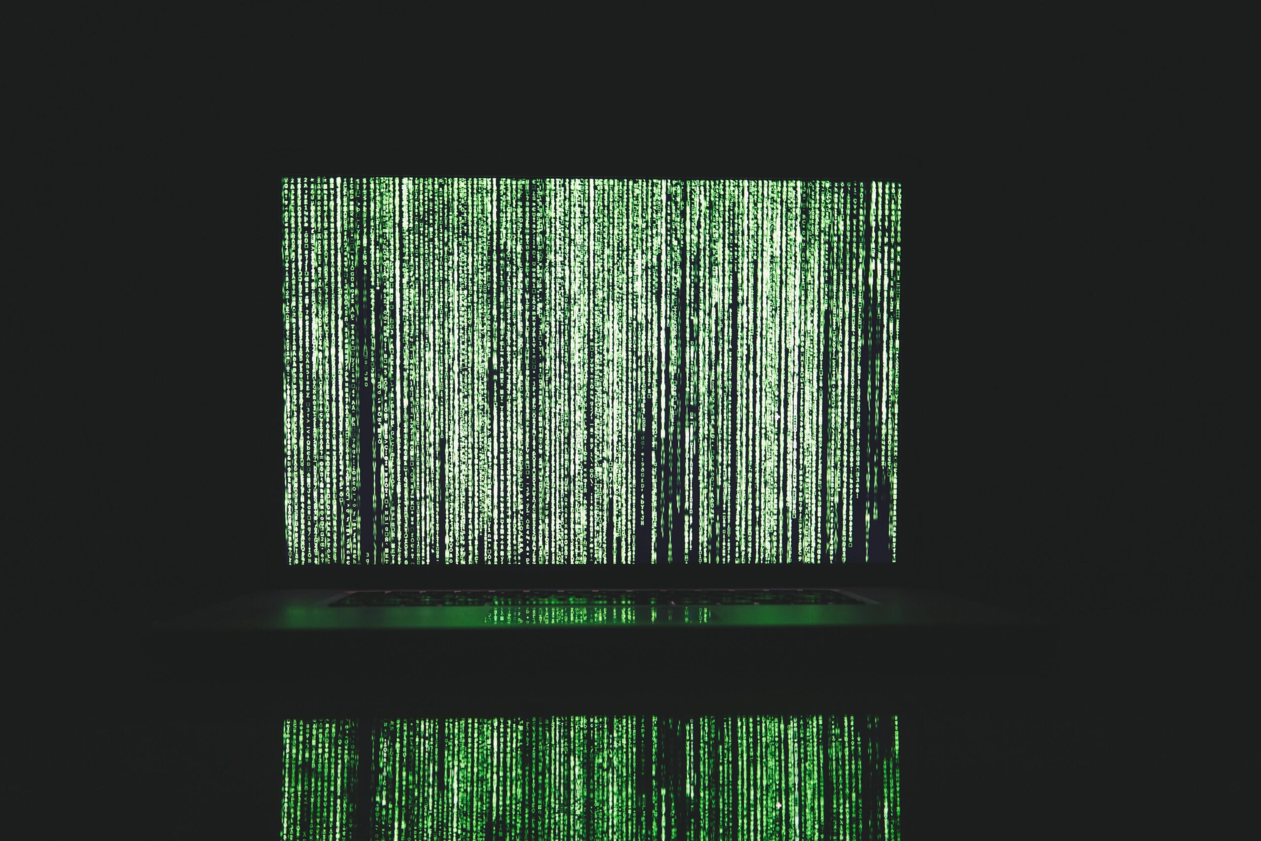 Laptop on a table displaying a green matrix code screen.