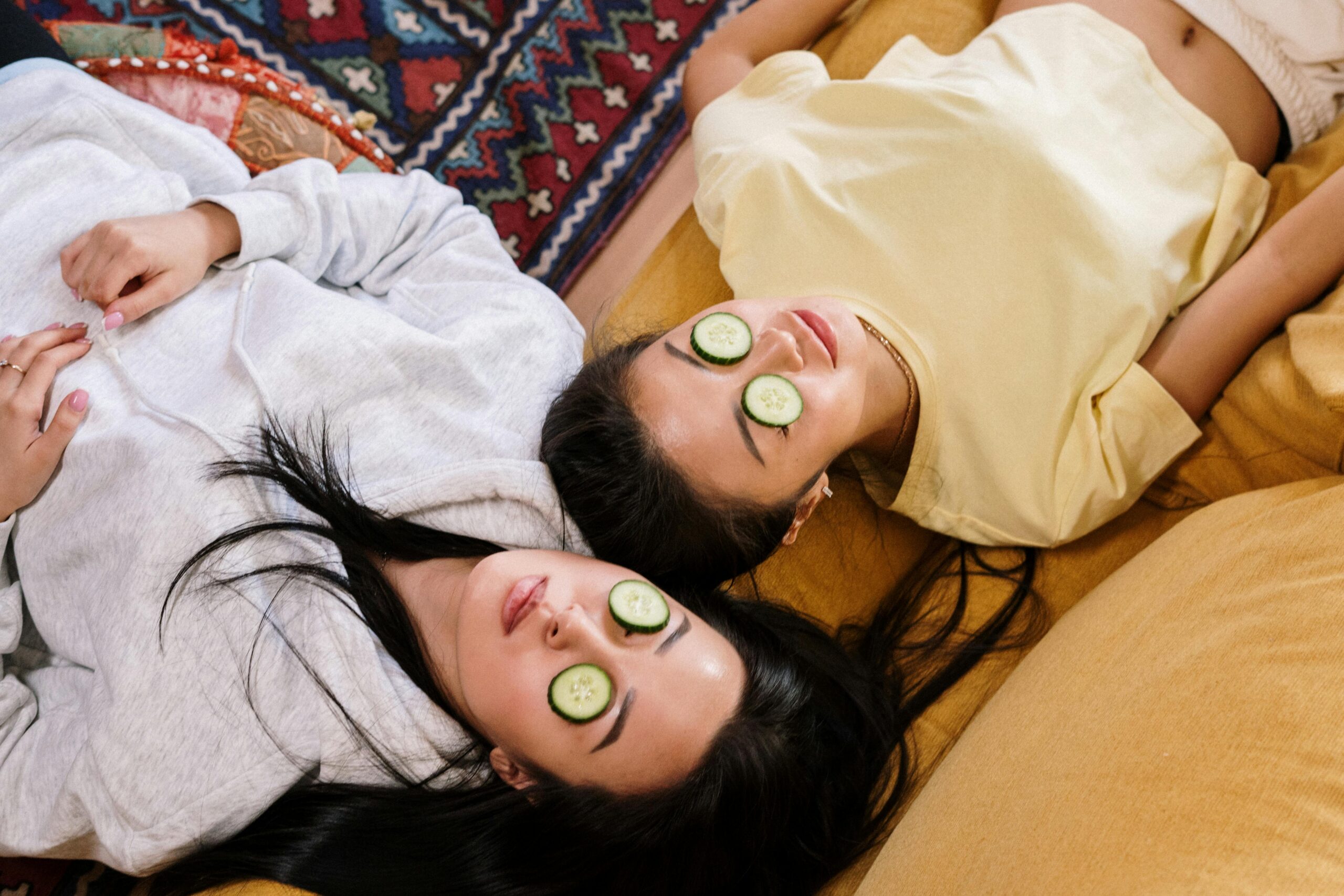 Two people lying down with cucumber slices over their eyes, relaxing.