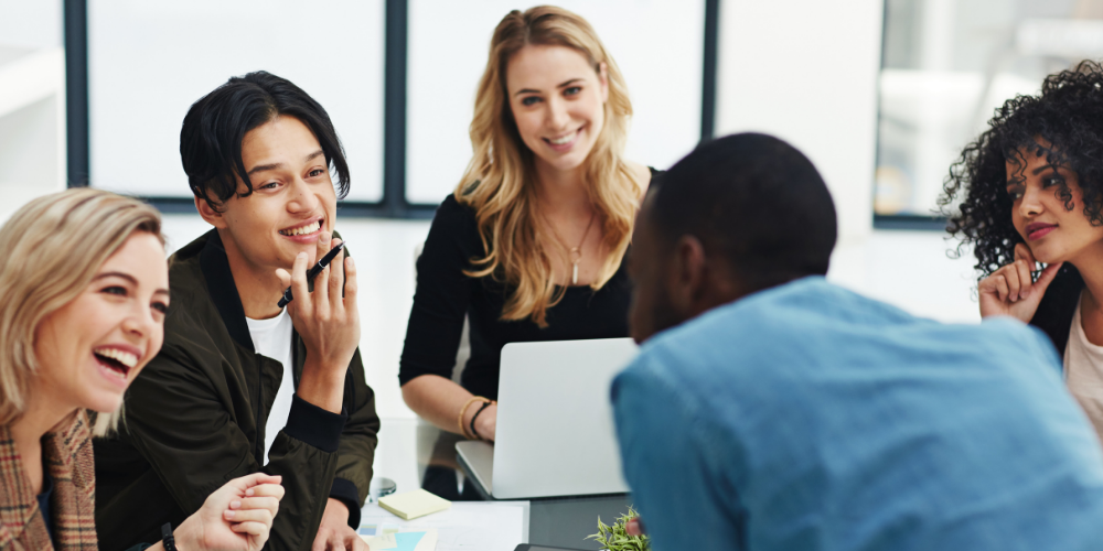 A diverse group of smiling professionals engaged in a meeting or discussion in a modern office setting.