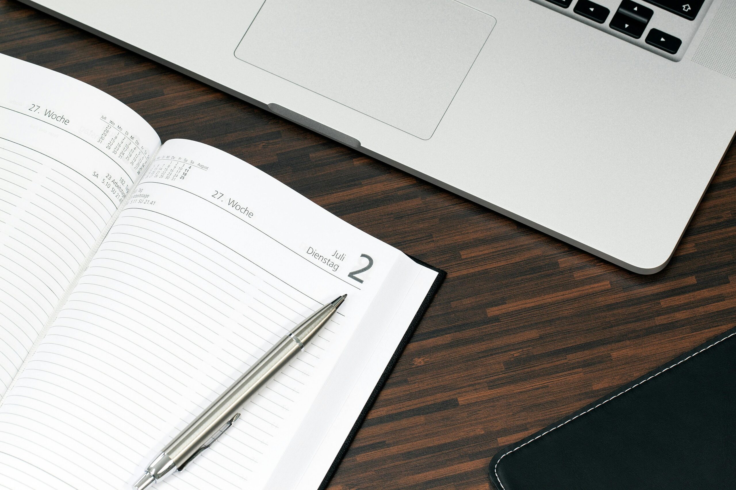 A close-up of an open, lined notebook and part of a laptop on a dark wooden surface.
