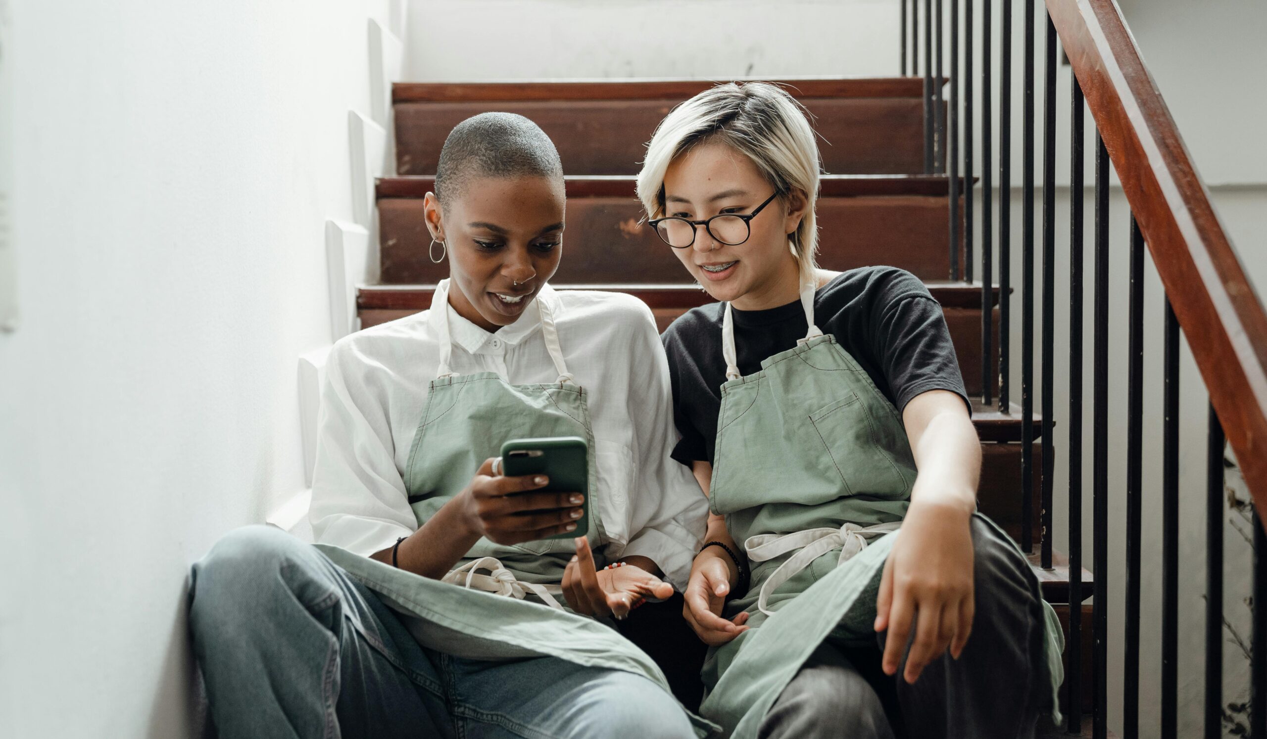 Two people sitting on stairs, looking at a smartphone together.