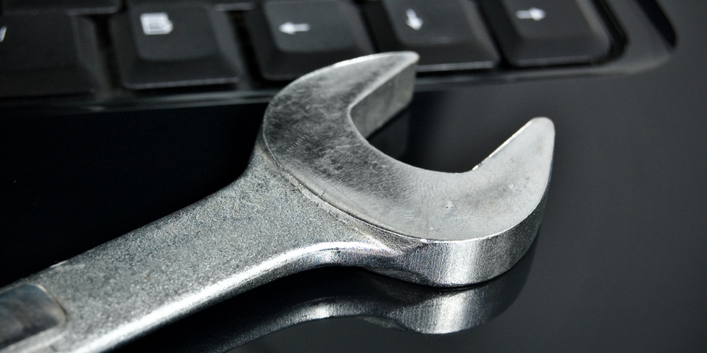 A close-up of a wrench laying on a computer keyboard, representing concepts like IT support, maintenance, or 'fixing' computer issues.