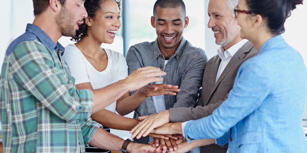 A team of professionals in a huddle, stacking hands together in a gesture of teamwork and collaboration.