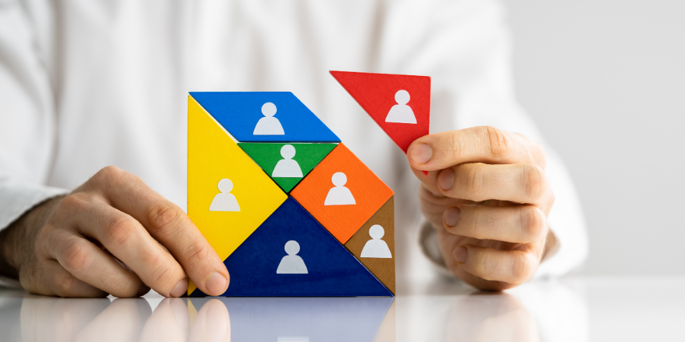 A person building a pyramid with colored blocks, each containing a silhouette of a person, suggesting team building or human resources management.