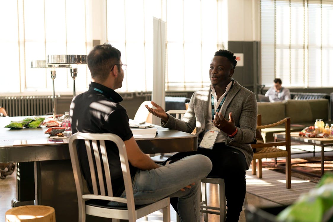 Two men seated at a table in a casual business setting, engaging in a discussion.