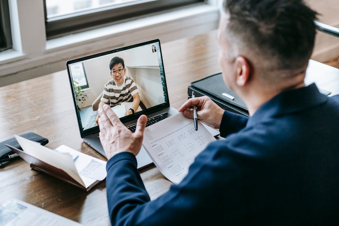 A professional in a blue blazer participating in a virtual meeting on a laptop in an office setting.