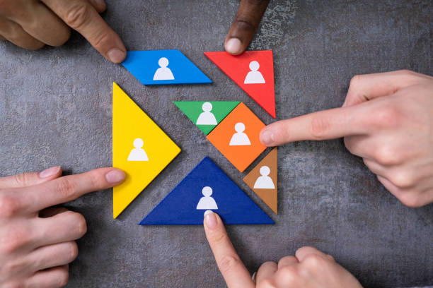 Several hands pointing to colorful triangular pieces with icons of people, possibly representing team diversity or assembling a team for a project.