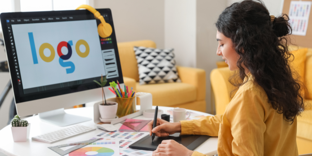 A young woman is working on a digital graphics tablet with a logo design on the screen, indicating a creative design process in a modern workspace.