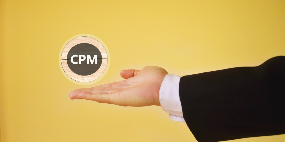 A person's hand presenting a wooden token with "CPM" in bold letters, suggesting a discussion of Cost Per Mille or Cost Per Thousand Impressions against a yellow background.