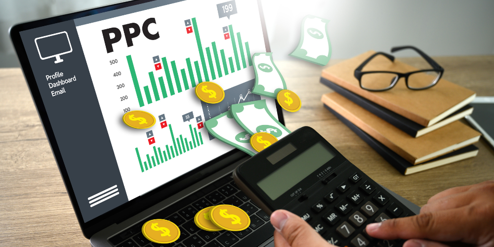 A person calculating costs on a calculator with a laptop screen showing graphs labeled "PPC" and currency symbols, indicating Pay-Per-Click advertising performance analysis.