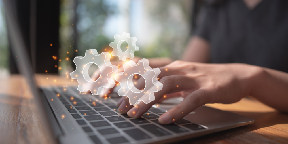 Close-up of hands typing on a laptop keyboard with glowing gear icons symbolizing automation or technology solutions.