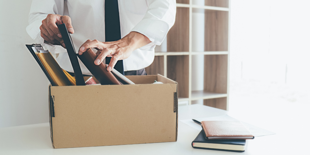 A person packing personal belongings into a box at an office, implying job termination or the end of employment.