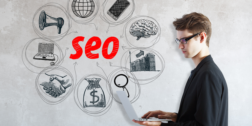 A young man in glasses working on a laptop with SEO-related sketches and concepts drawn around him.