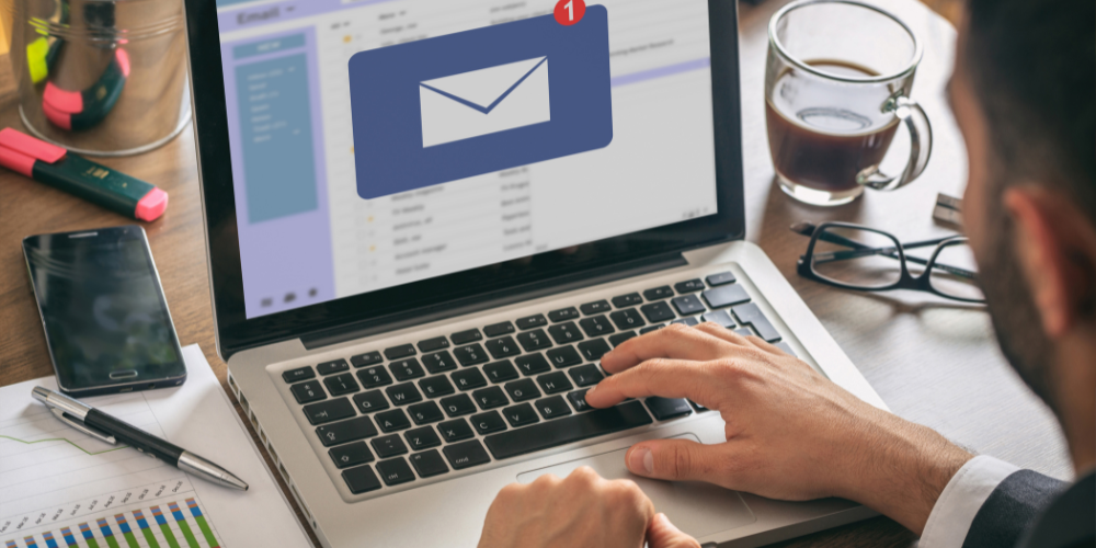 A close-up of a man's hands typing on a laptop with an email notification on the screen, indicating online communication or work.