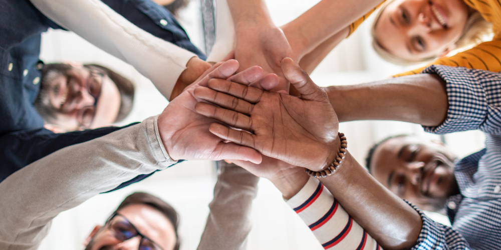 A group of people stacking hands in the center, representing teamwork or unity.