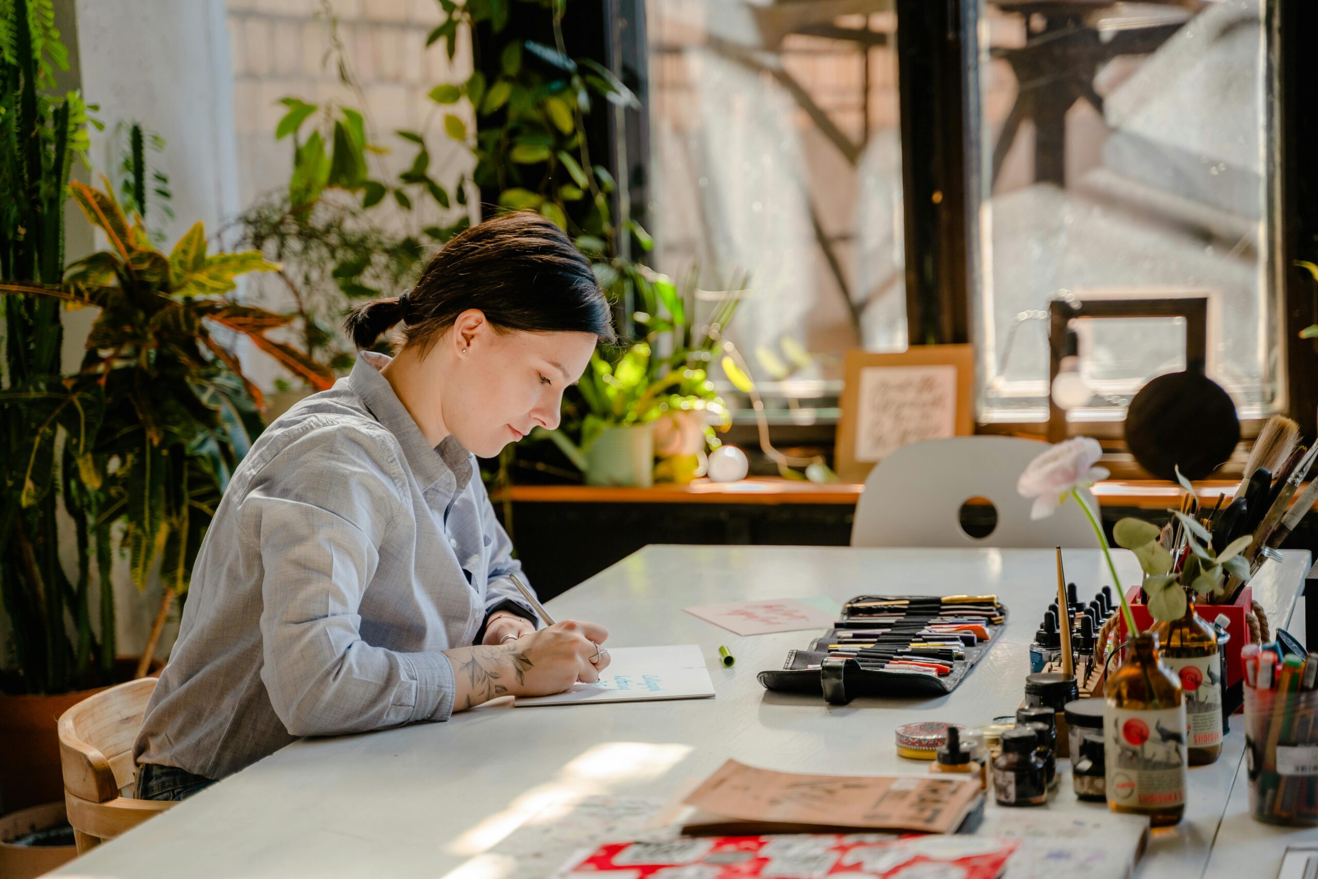 Artist sketching in a sunlit studio surrounded by art supplies.