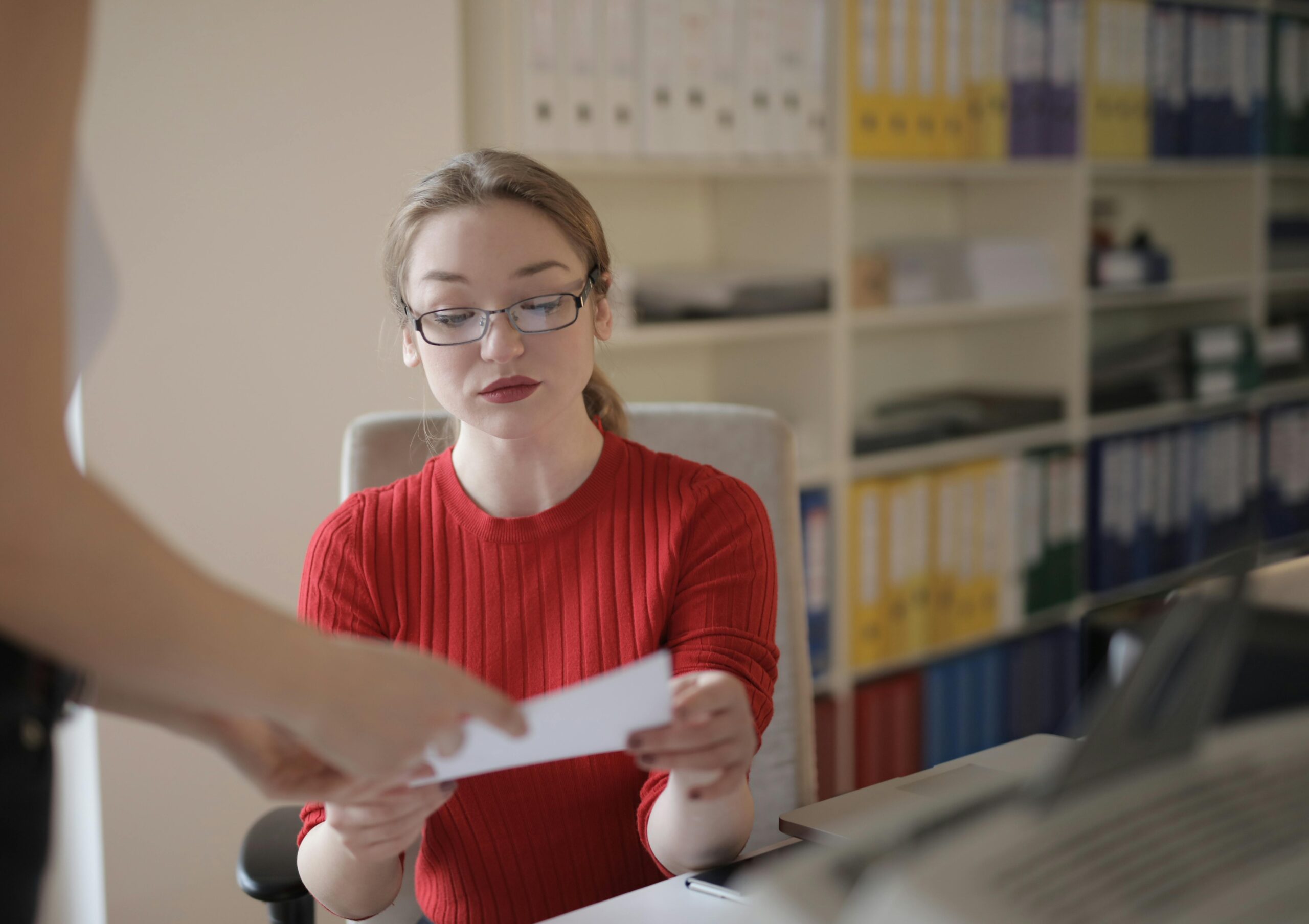 A woman in red attentively reviewing a document handed to her, exemplifying the detailed evaluation process of candidates by staffing firms and how they work to find the right fit for employers.