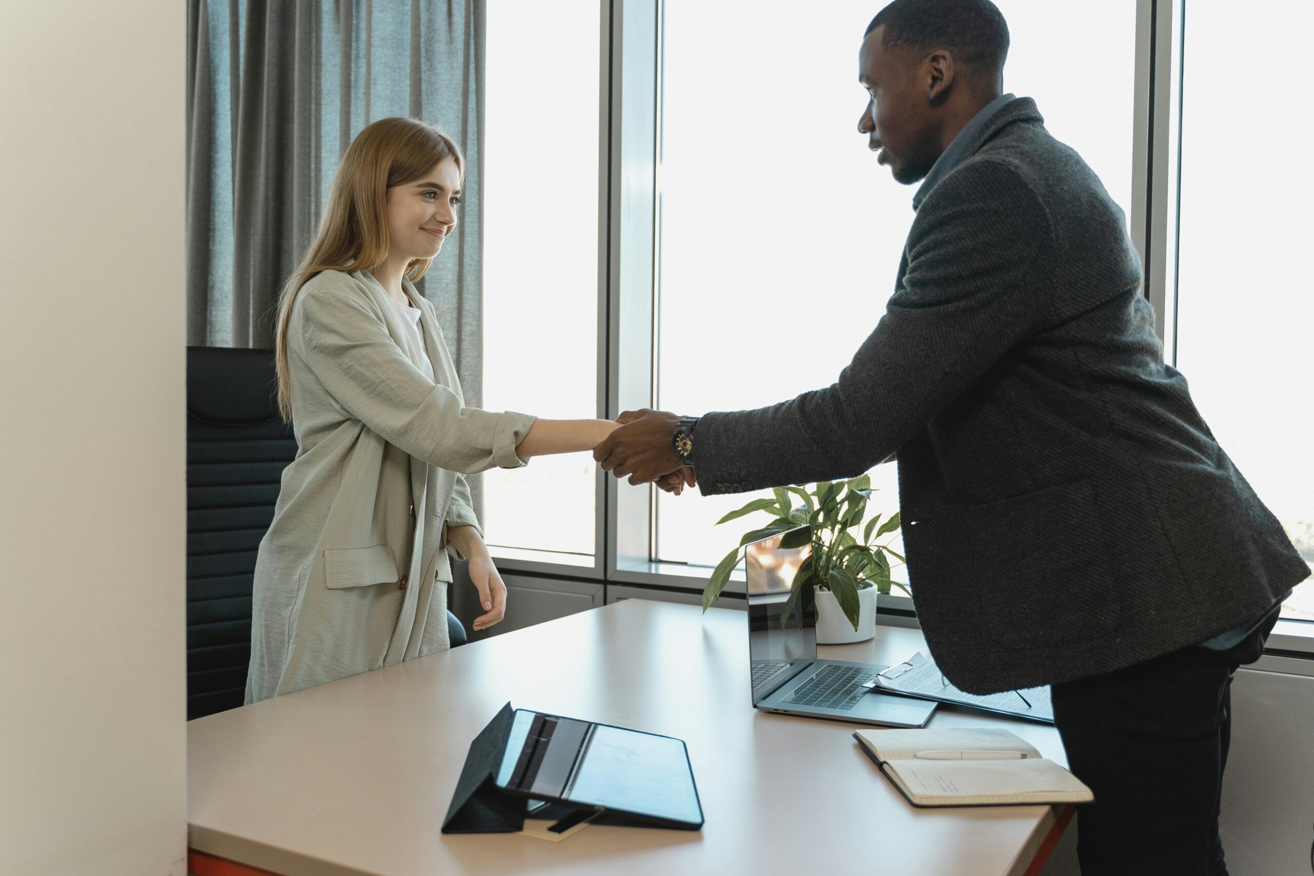 Two businesspeople shaking hands in a well-lit office, representing the mutual agreements in what is recruitment outsourcing.