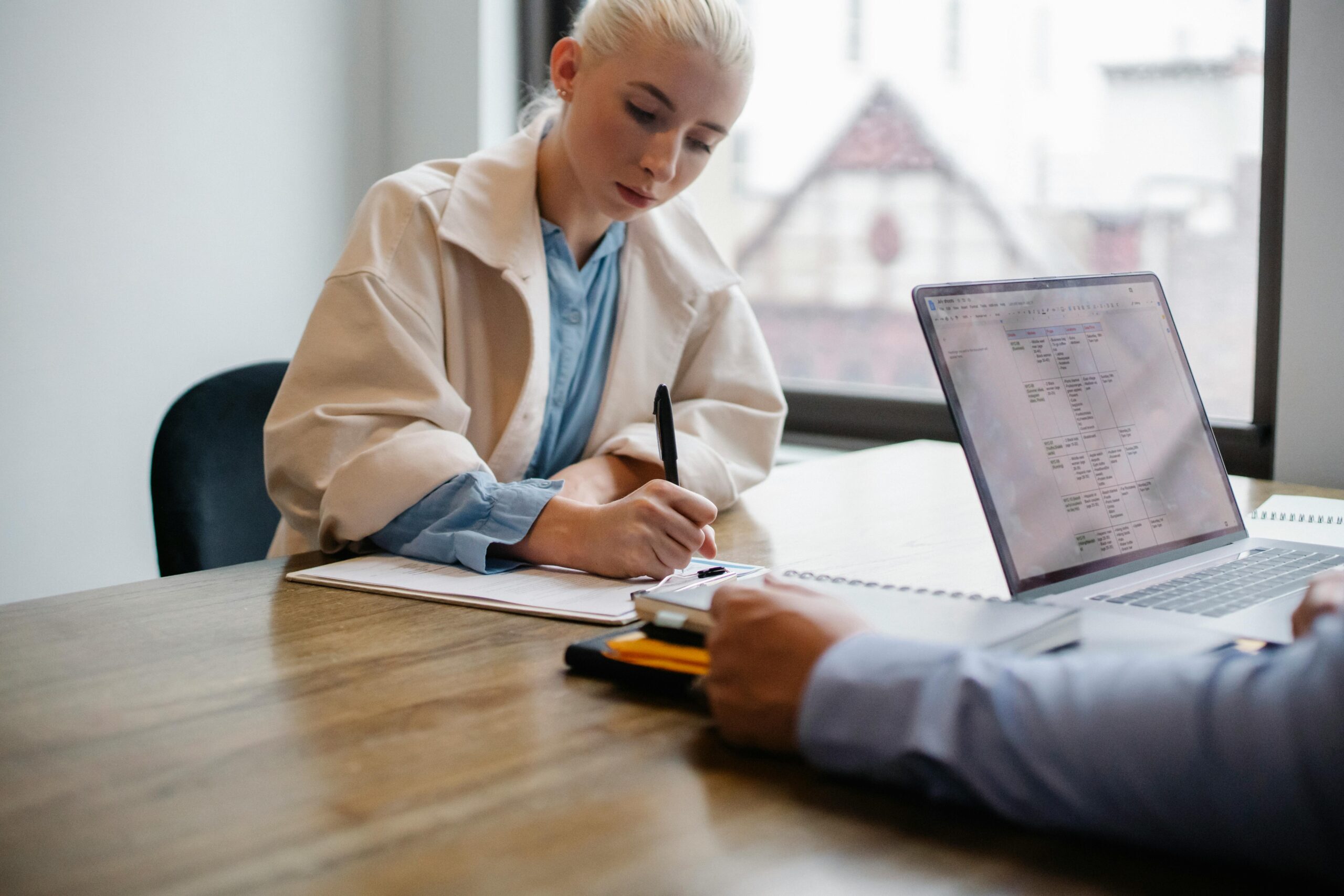 In a meeting room, a personal assistant notes important details, possibly about the salary for a personal assistant, on her notepad.