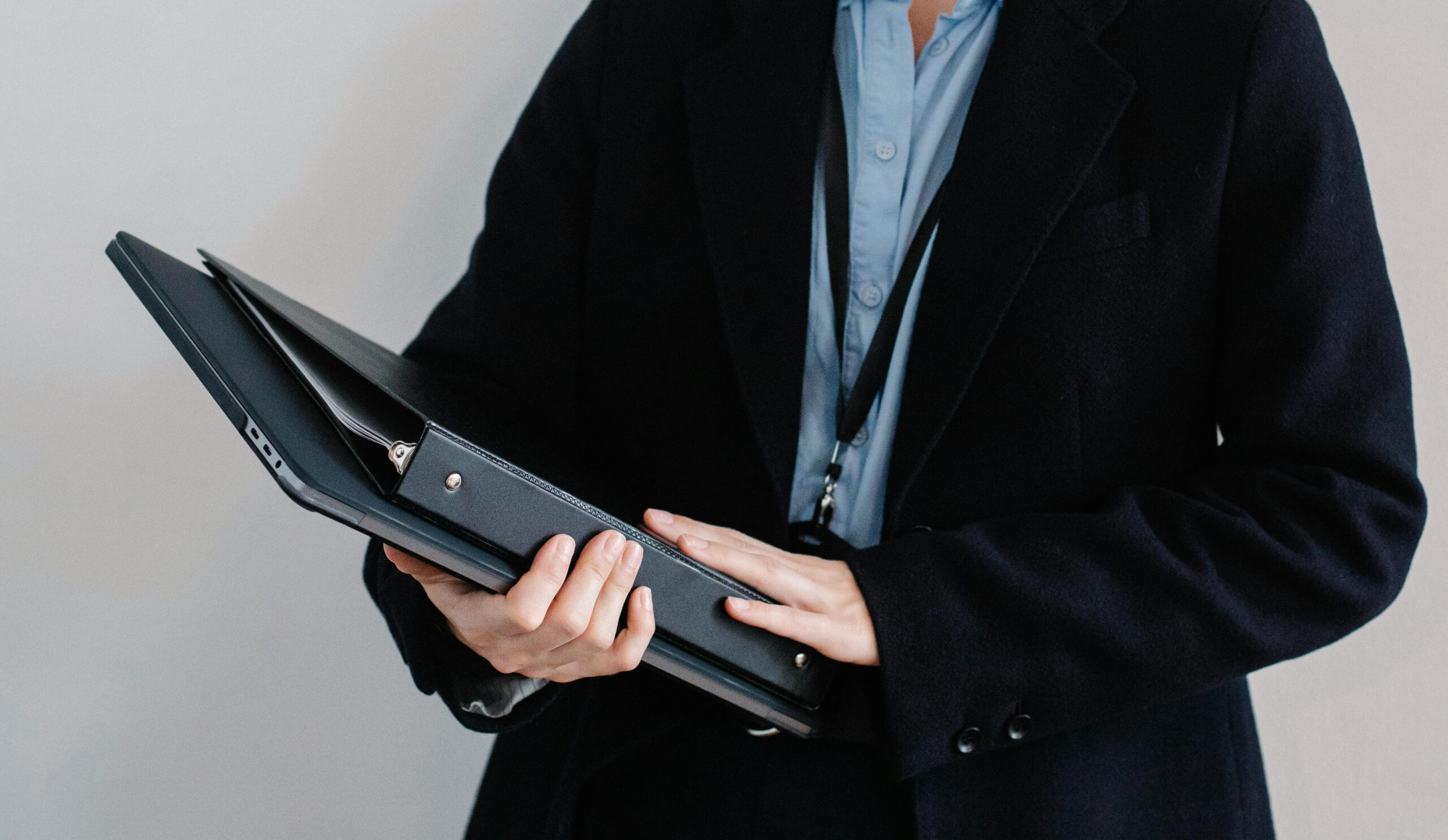 A professional personal assistant in a black coat holds a leather portfolio, considering documents about the salary for a personal assistant.
