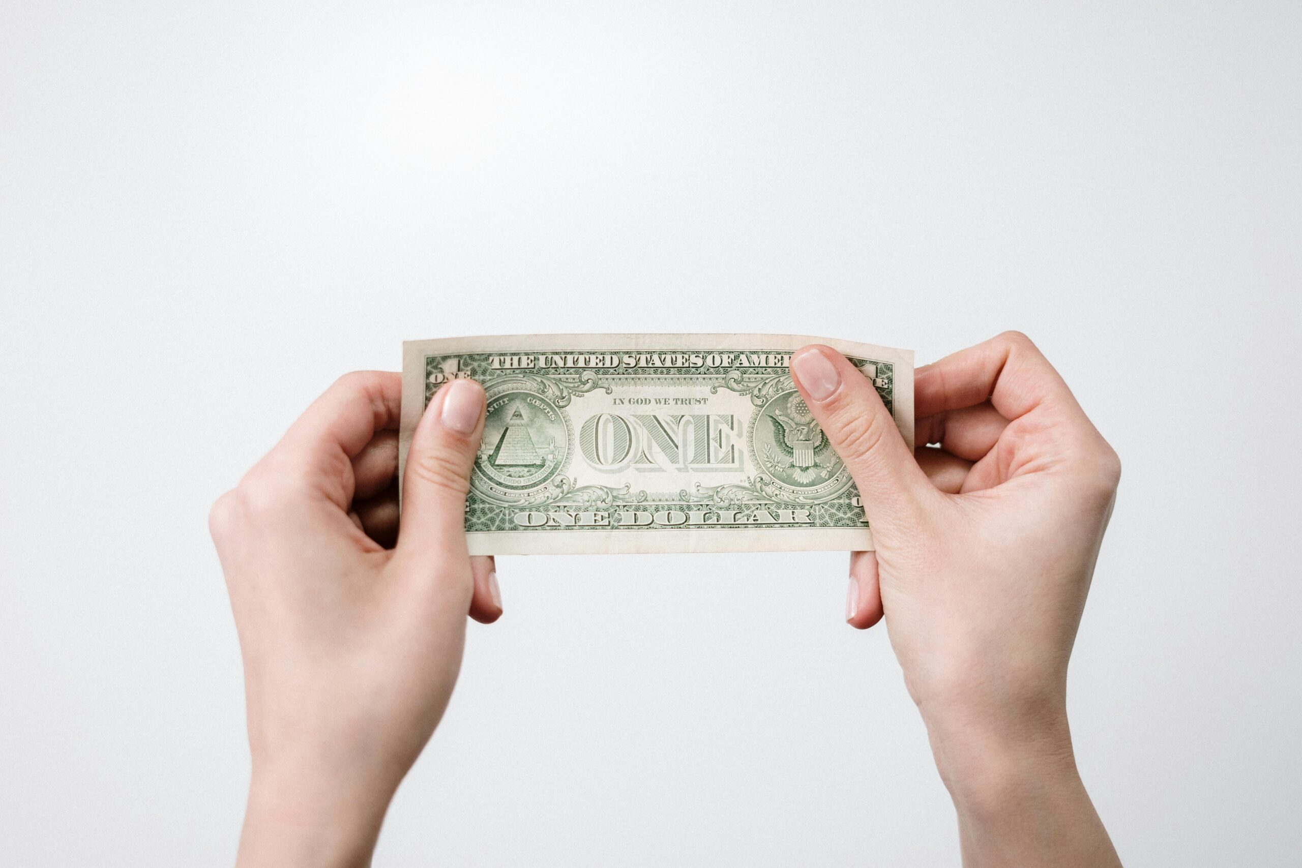 Hands holding a stretched one-dollar bill, representing the financial considerations when choosing a professional summary generator.