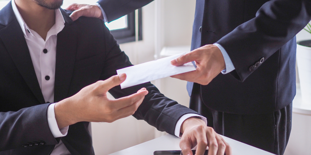 An employer handing a paycheck to his employee across a table in an office.