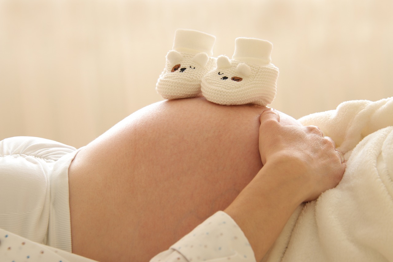 A pregnant person resting, with baby shoes on their belly.