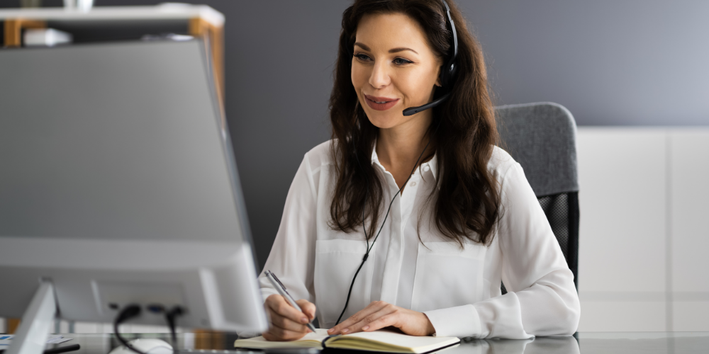 A focused woman wearing a headset, writing notes, indicative of a customer support or telecommunication role.