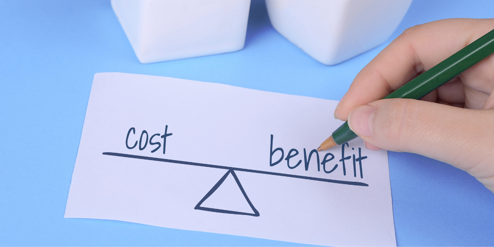 A hand writing a cost-benefit analysis on a piece of paper, with a balance drawn beneath the words.